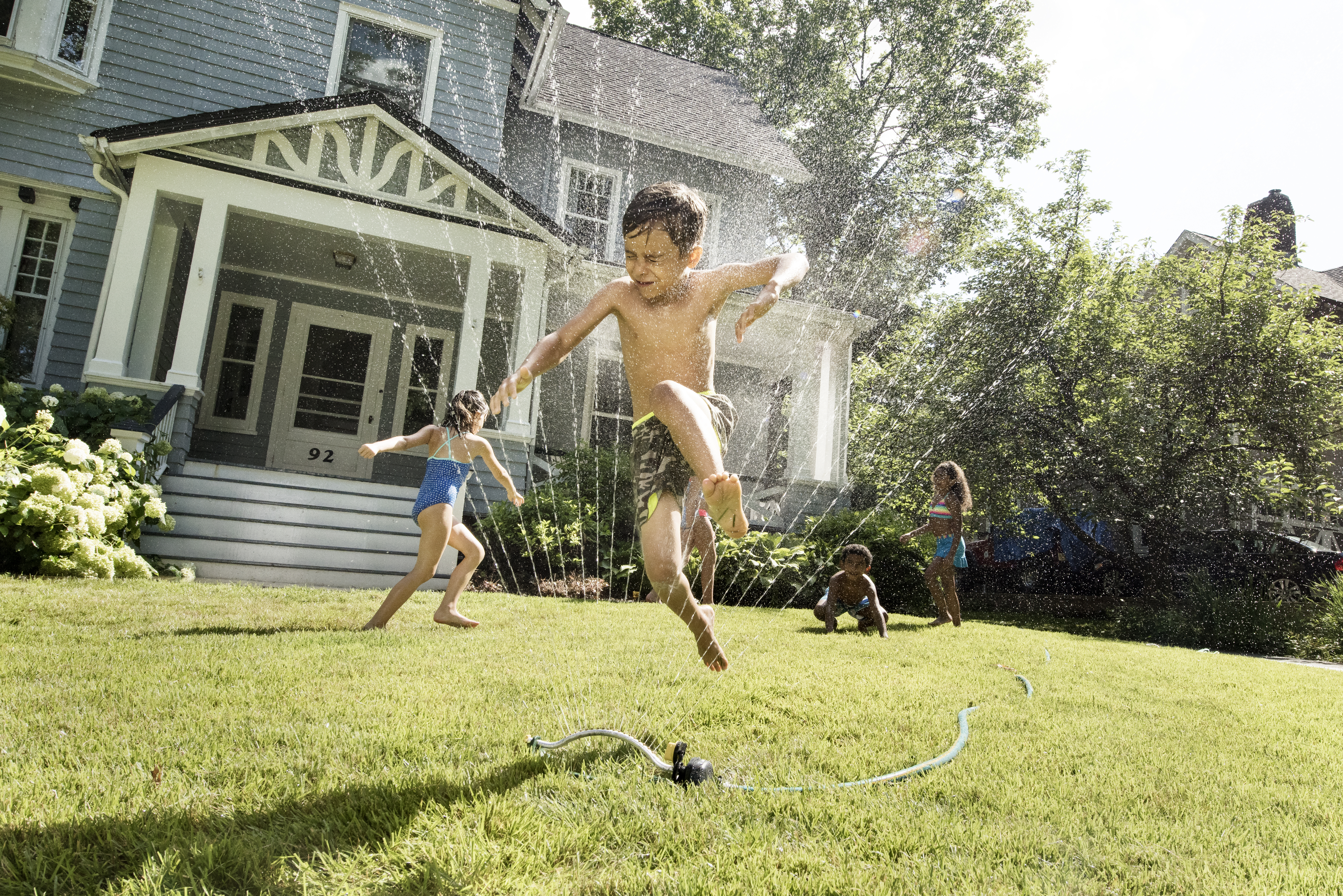 Kids playing joyfully with water sprays in front yard
